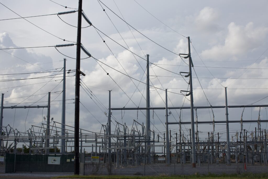 A grey AEP Texas electrical substation behind a fence against a blue sky with clouds in McAllen, Texas.