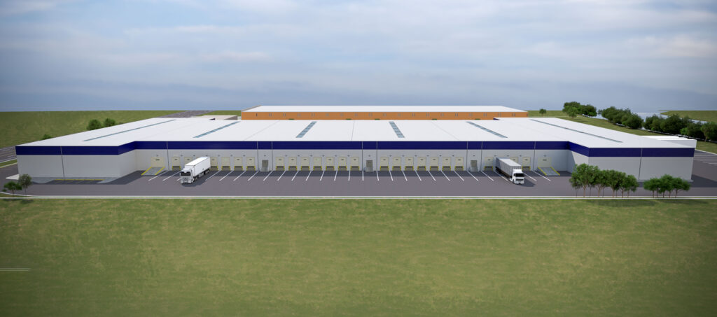 A large blue and white warehouse with dozens of trucking bays sits near green fields with trees under a blue and white sky.