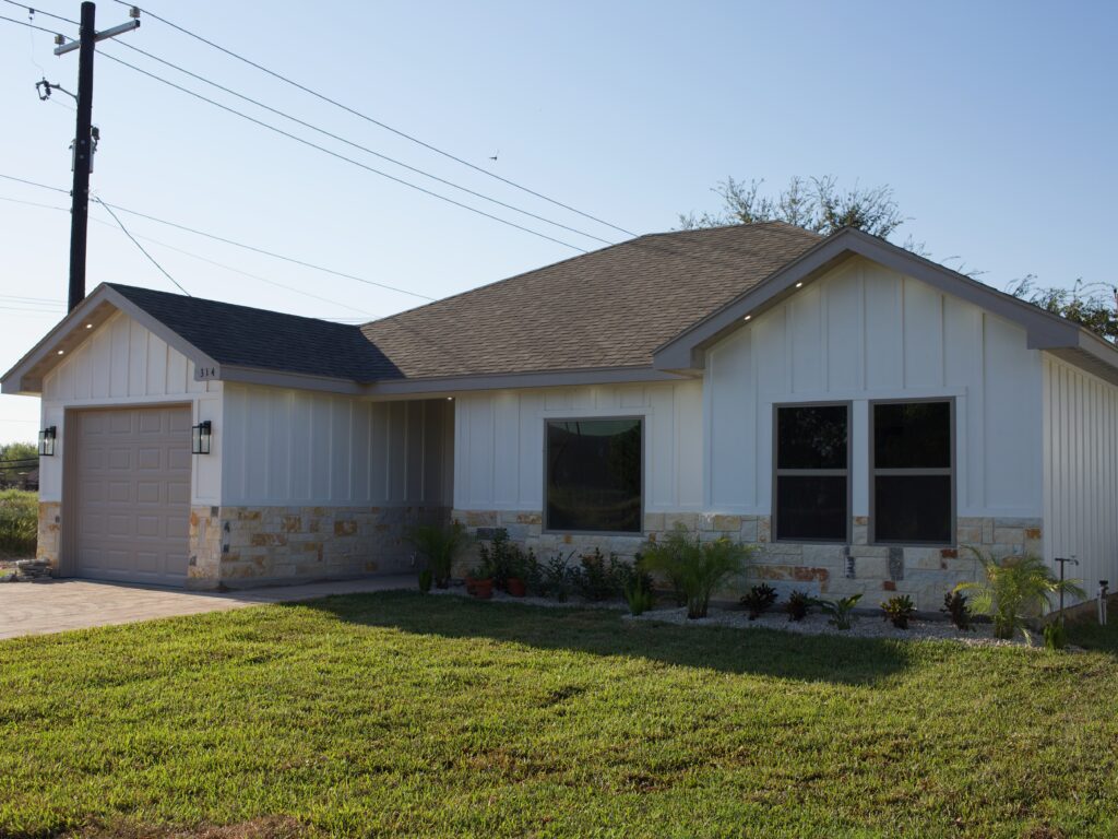 A white sided home with stone facade and a green grass yard sits beneath a blue sky.