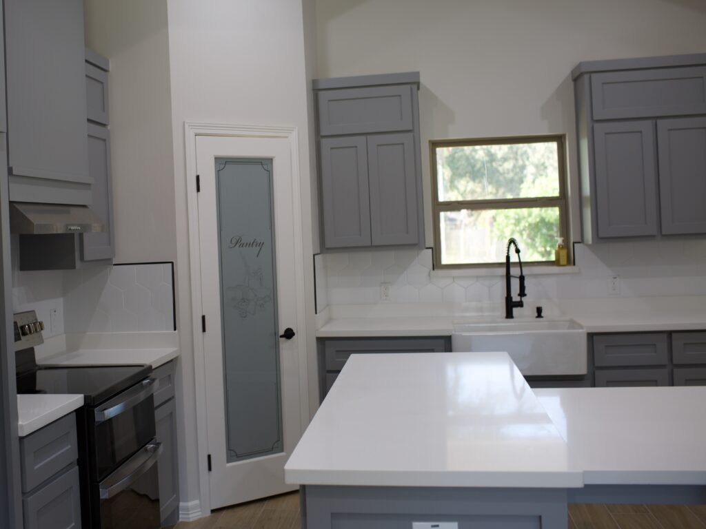 A white and grey kitchen includes a stove, countertop, sink and cabinets.