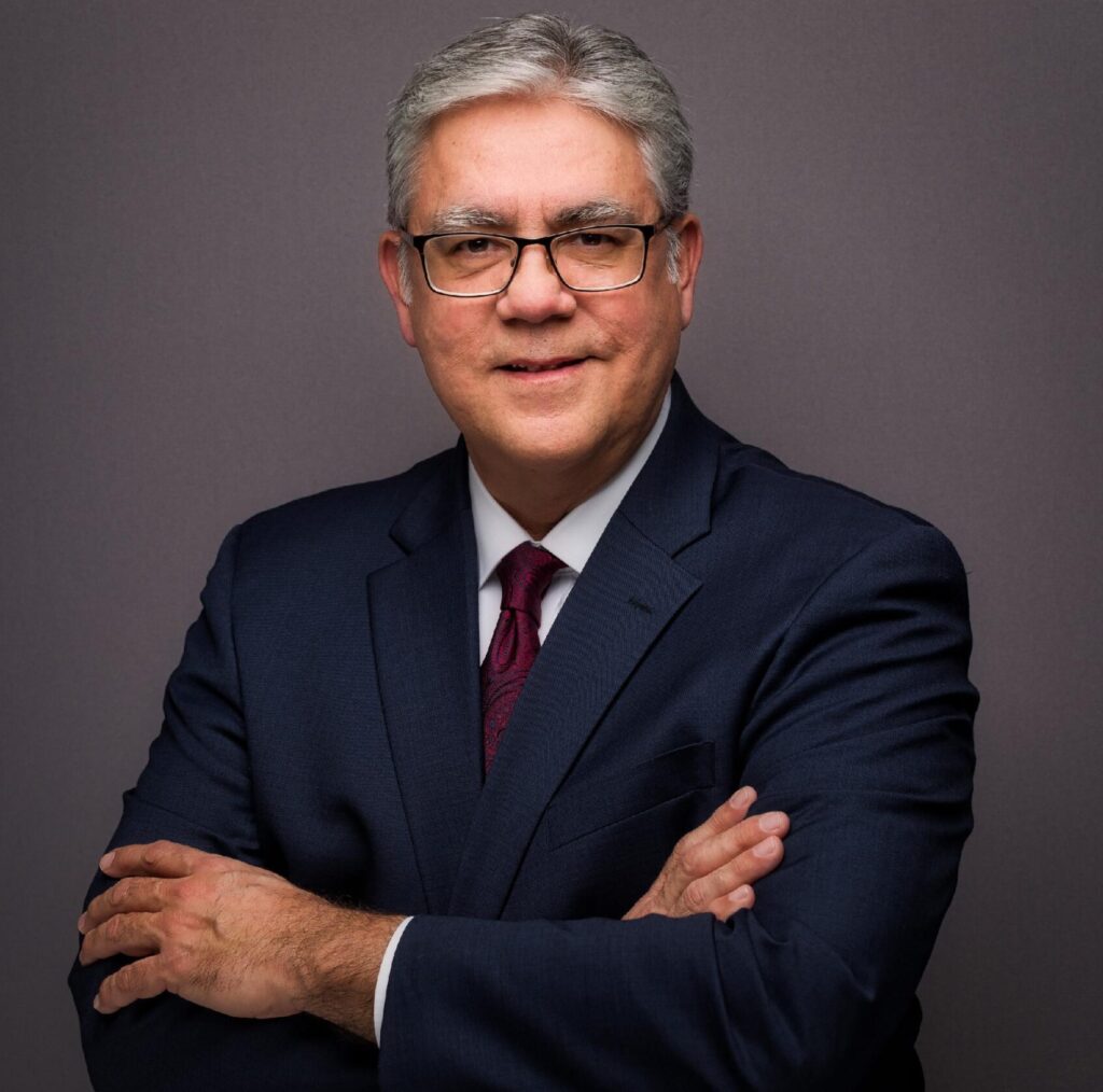 Steven M. Valdez is in a blue suit with a white shirt and a maroon tie.