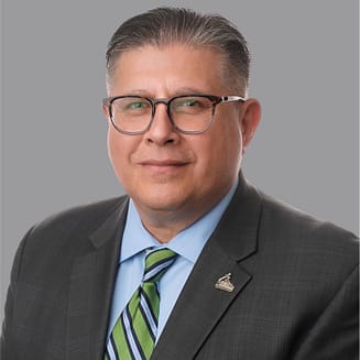 Headshot of Teclo Garcia, the CEO of Mission EDC, in a grey suit with glasses.