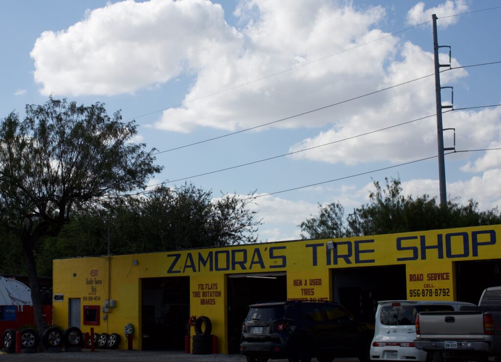 A yellow automotive shop sits on the corner with an electric transmission pole in the background with a blue sky.