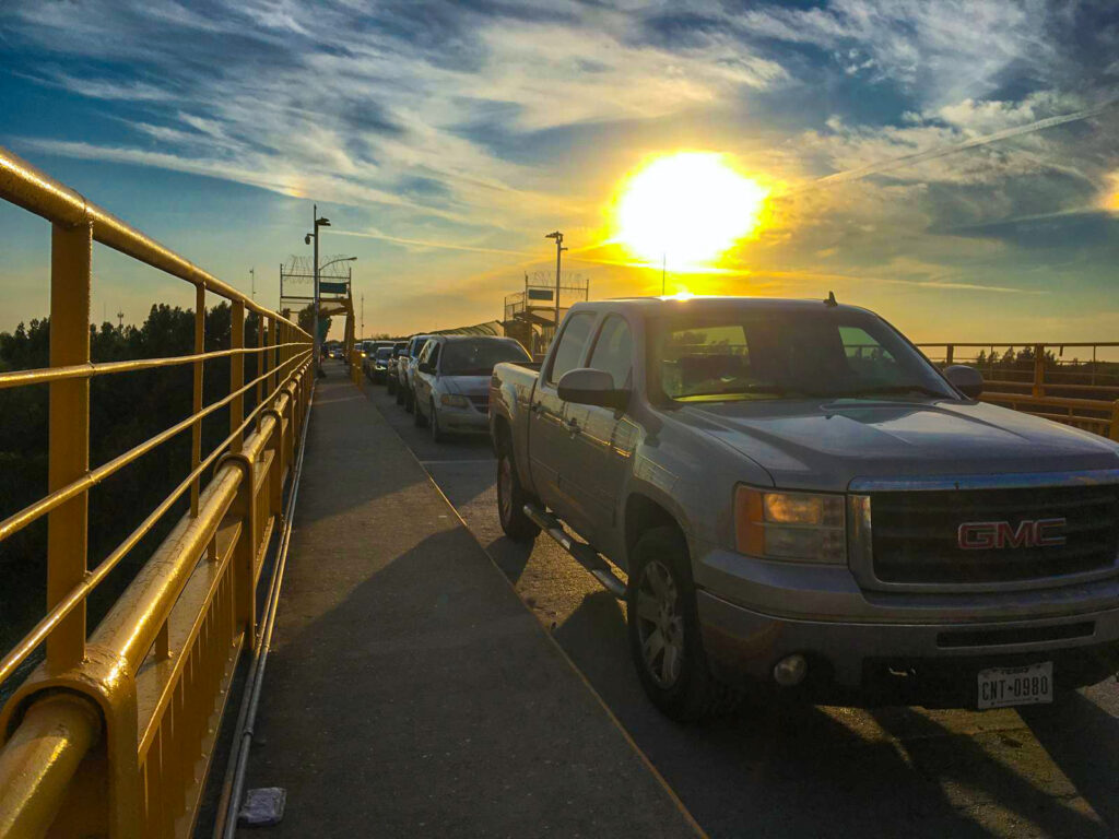 Pickup trucks and cars wait in line on the Starr Camargo Bridge at sunset.