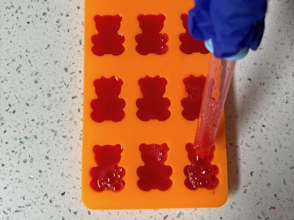 A close-up of a gloved hand using a liquid dropper to fill a Boosties gummy mold.
