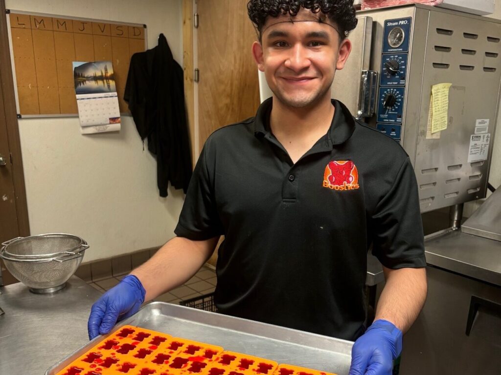 A male teen wearing a hair net and gloves showcases sugar-free energy gummy bears in their molds.