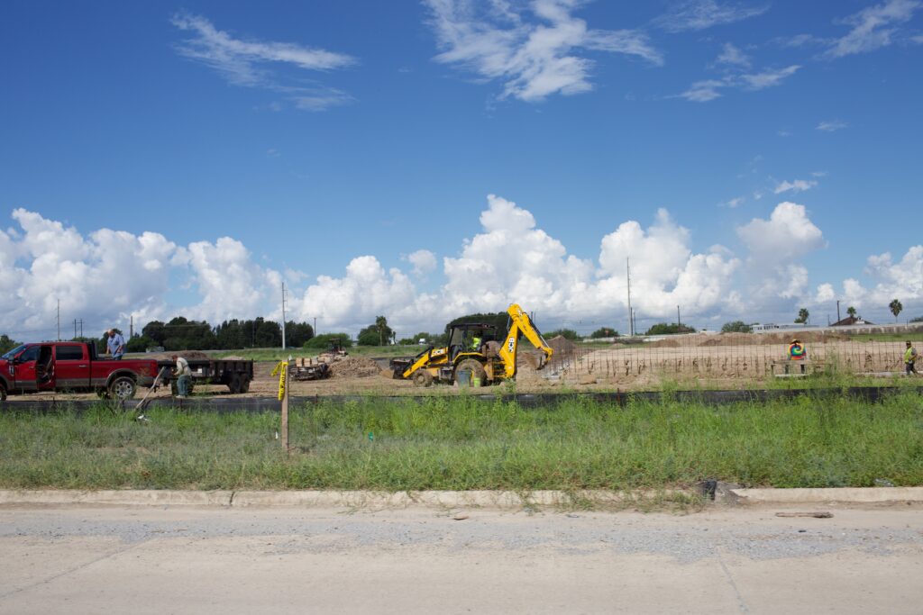 Construction workers in grass beneath a blue cloudy sky.