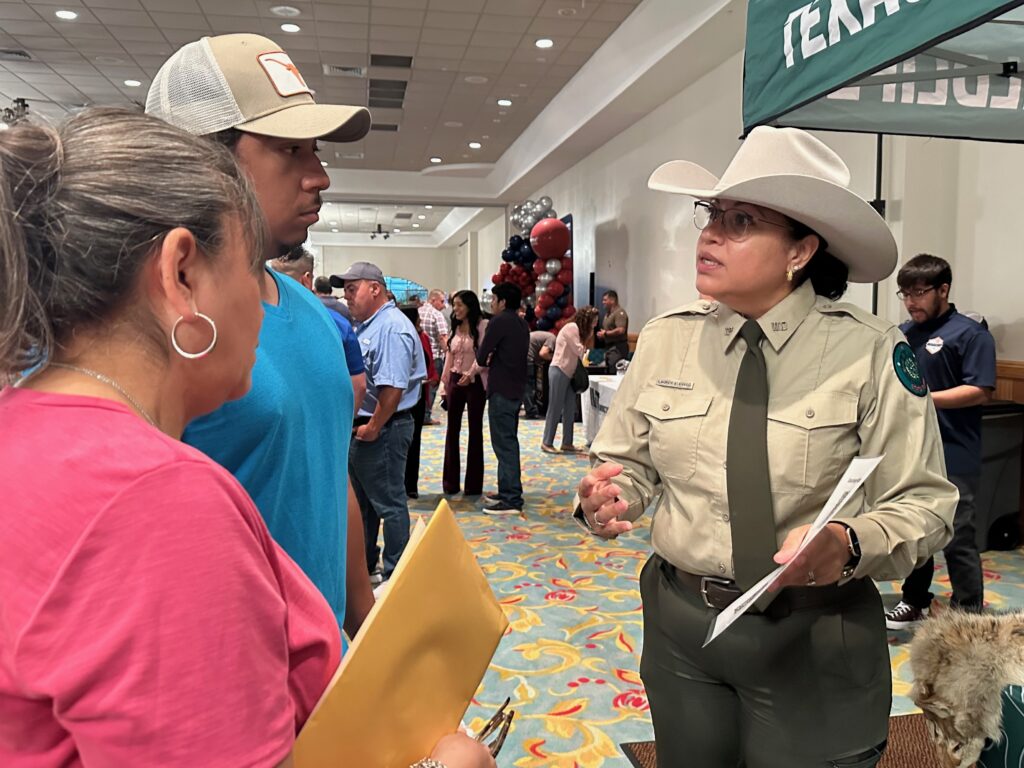 Texas Game Warden in uniform speaking with two attendees at the Brownsville job fair.