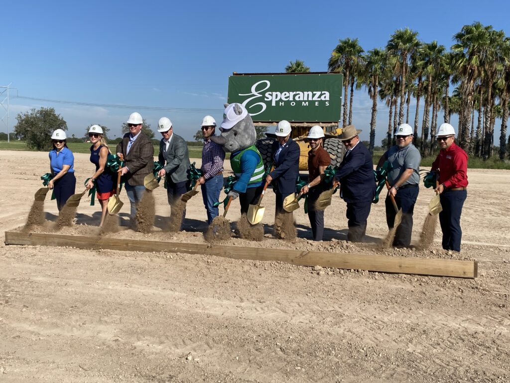 A line of people wearing hard hats and holding gold shovels toss dirt at the La Sienna groundbreaking in Edinburg, Texas.