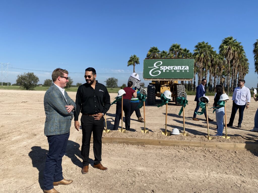 Nick Rhodes, wearing a suit jacket and sunglasses, talks with an Esperanza Homes team member near ceremonial shovels and an Esperanza Homes sign after the La Sienna groundbreaking in Edinburg, Texas.