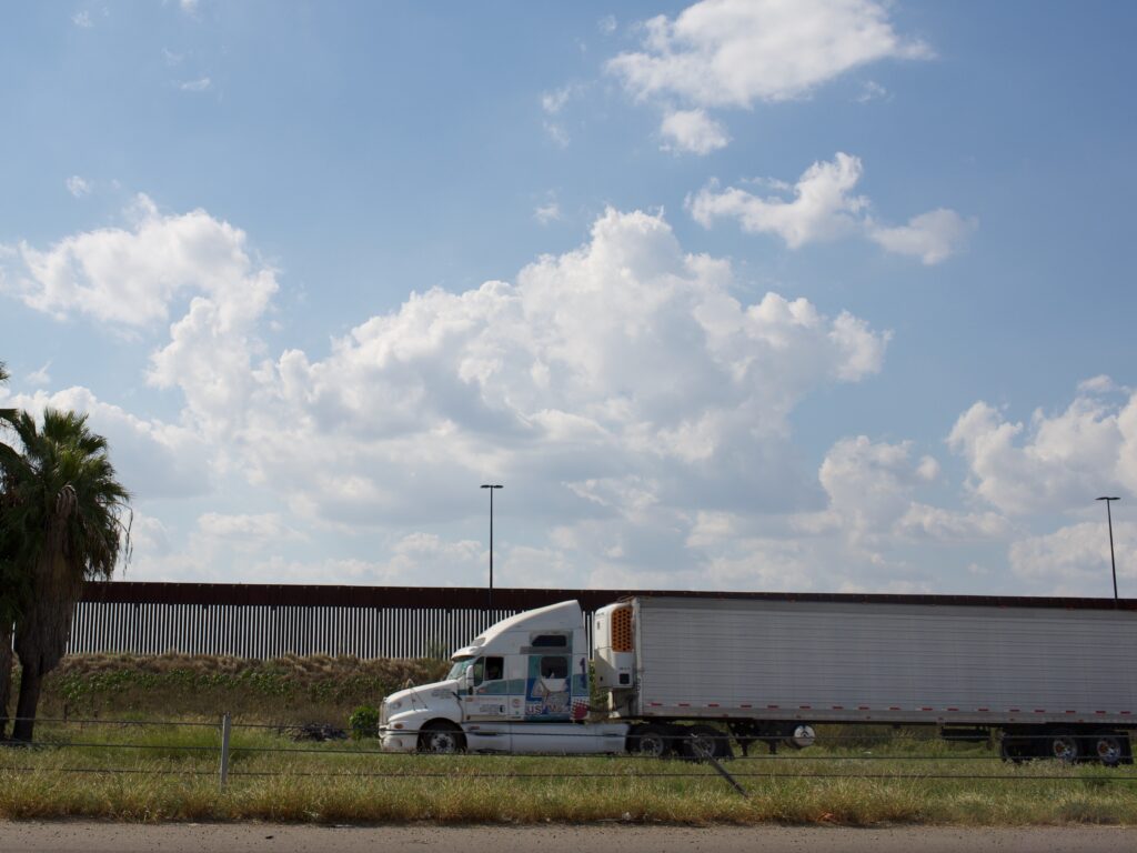 A tractor trailer drives along the U.S.-Mexico border wall.