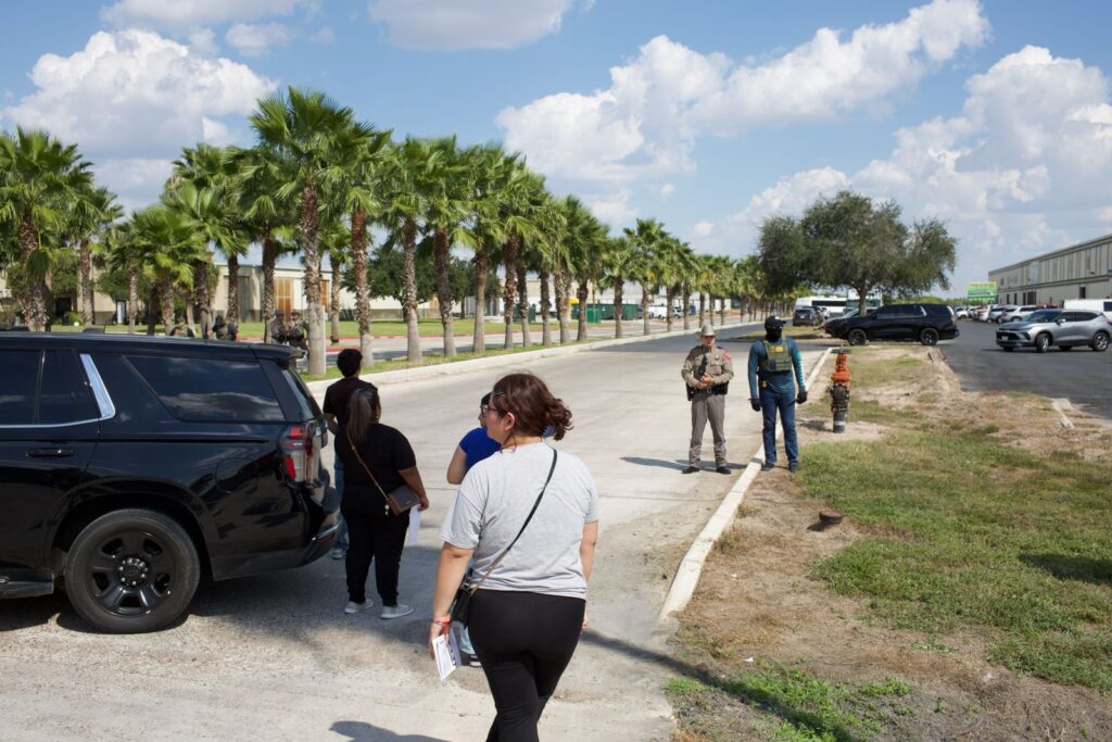 ICE agents and DPS troopers secure the perimeter outside the Tres Dimensiones Ropa Usada warehouse in McAllen on Thursday as onlookers gather nearby. 
