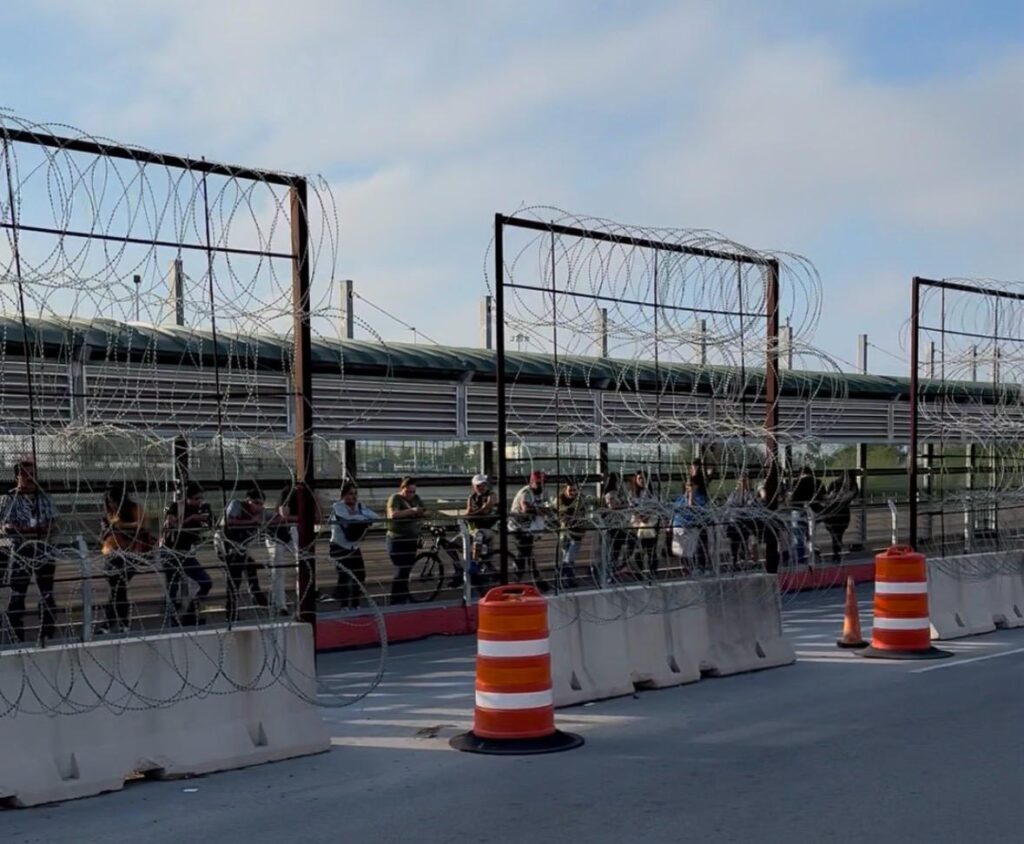 People stand in line behind fencing and barriers at the McAllen-Hidalgo International Bridge in September 2025.