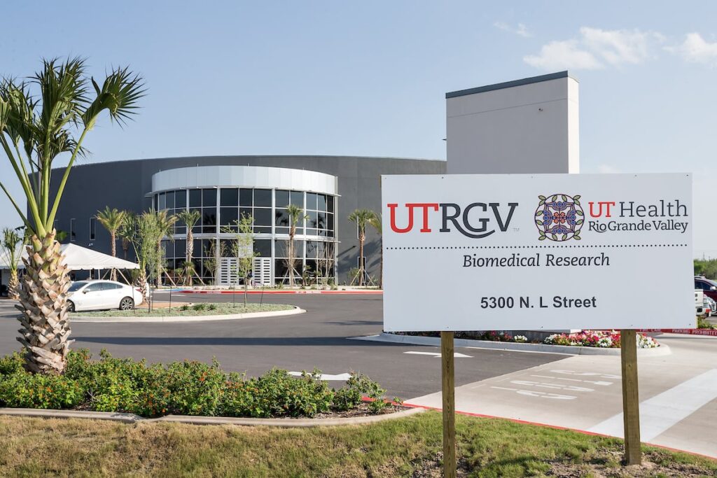 UTRGV Biomedical Research Building in McAllen Alt text: Exterior of the UTRGV Biomedical Research Building in McAllen, showing its curved glass façade and palm-lined entrance.