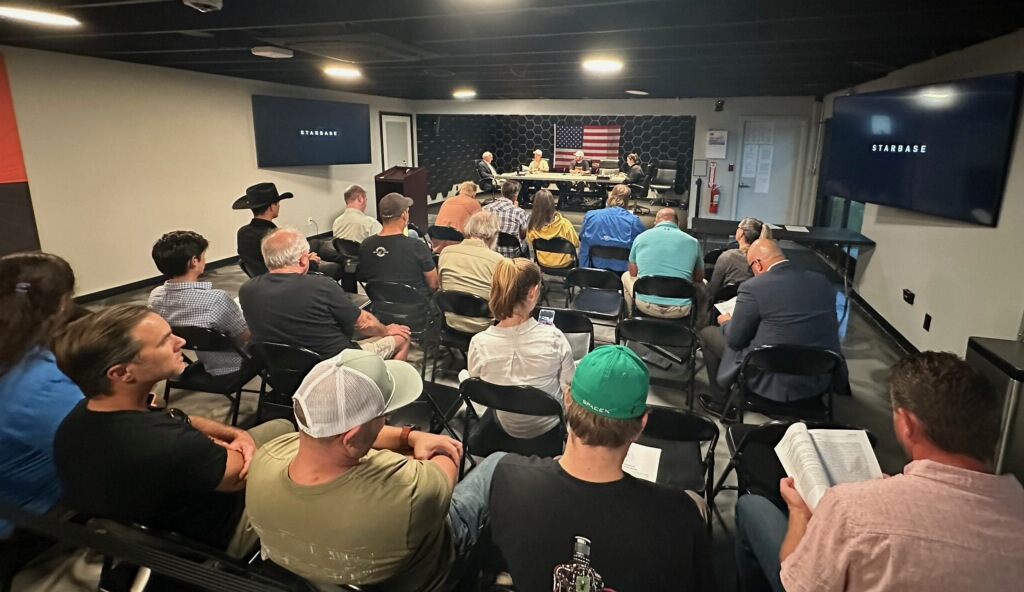 Audience members seated inside the Starbase City Council chambers during a public meeting, with officials visible at the front of the room.