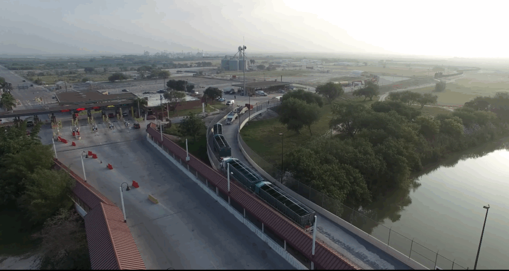 Aerial image showing trucks entering commercial inspection lanes at the Progreso International Bridge with cargo facilities in the background.