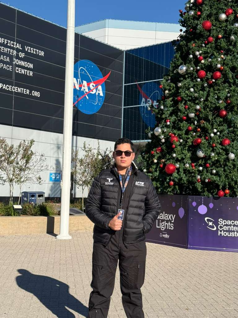 Jesús Sebastián Moreno García standing in front of the NASA logo at Space Center Houston next to a decorated Christmas tree.