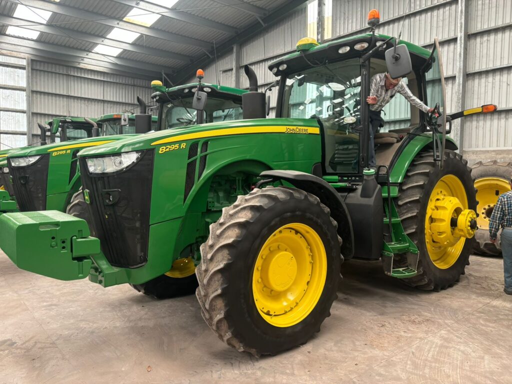 Large green John Deere tractors parked inside a metal equipment shed.