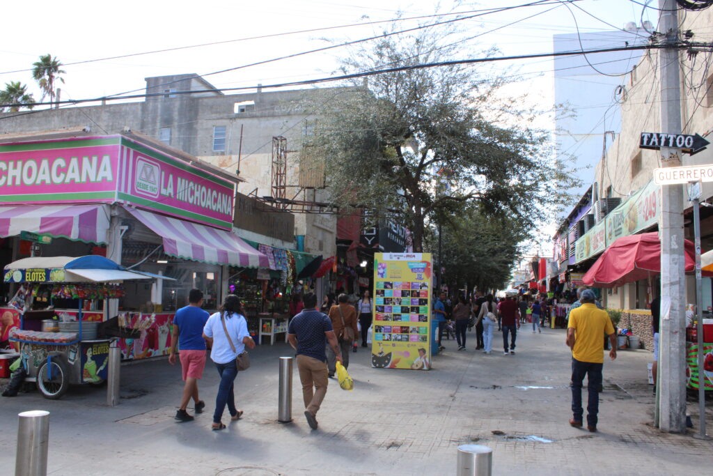 Pedestrians walking along a commercial street in Reynosa’s downtown area with small shops and vendor stands.