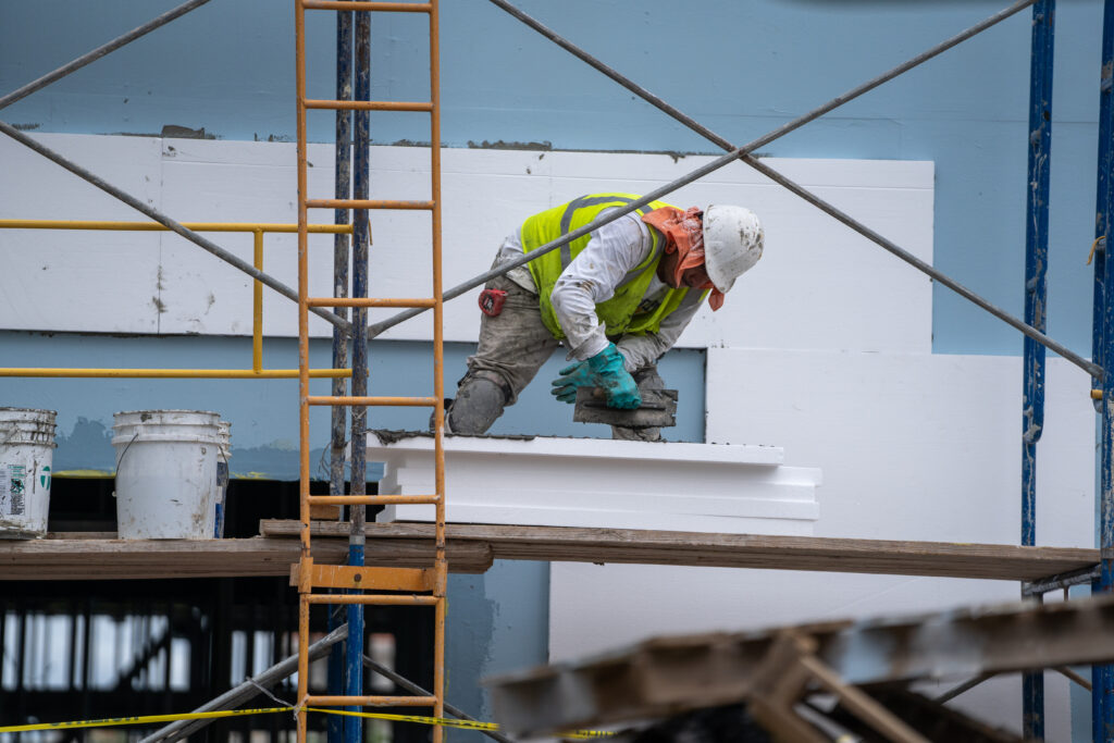 Construction worker on scaffolding applying material to an exterior wall at an Edinburg construction site.