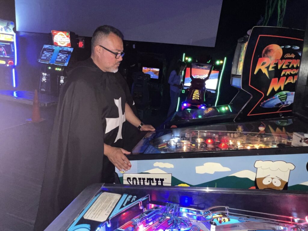 Man playing a themed pinball machine in a dimly lit arcade at Space Monkey Barrcade.