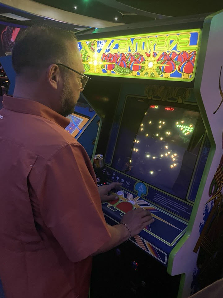 Man standing at a vintage Centipede arcade machine inside Space Monkey Barrcade.
