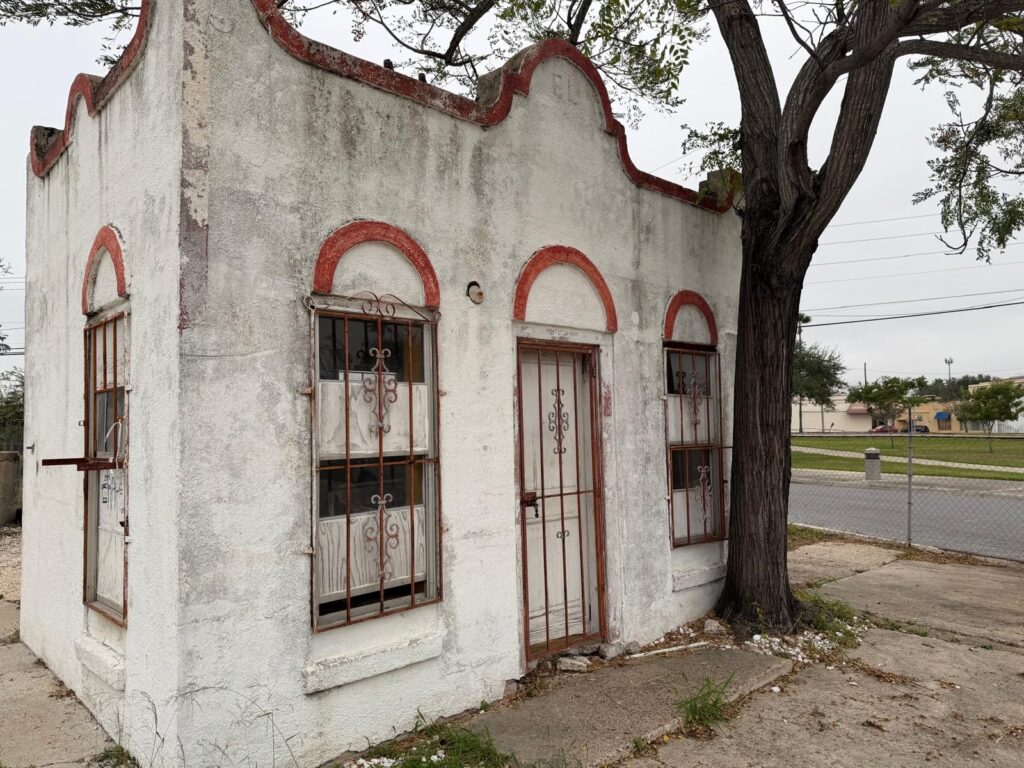 A weathered historic building with barred windows and a tree beside it in downtown Harlingen.
