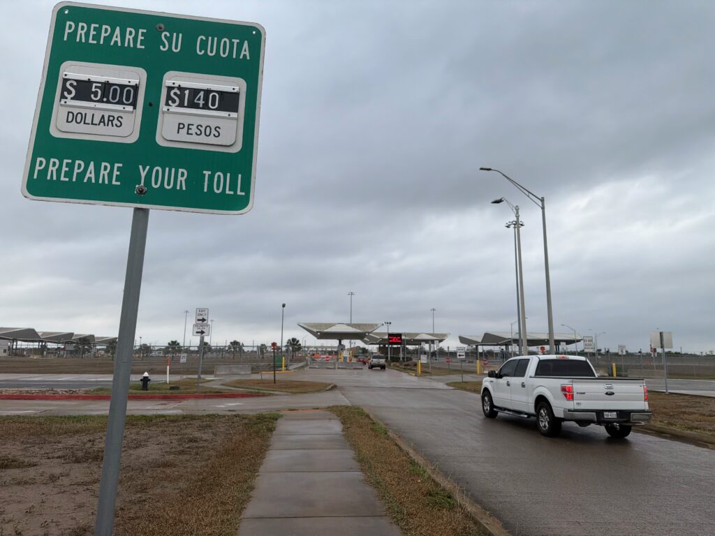 Green toll sign showing $5 and 140-peso rates with cars driving toward the Donna bridge’s port-of-entry booths.