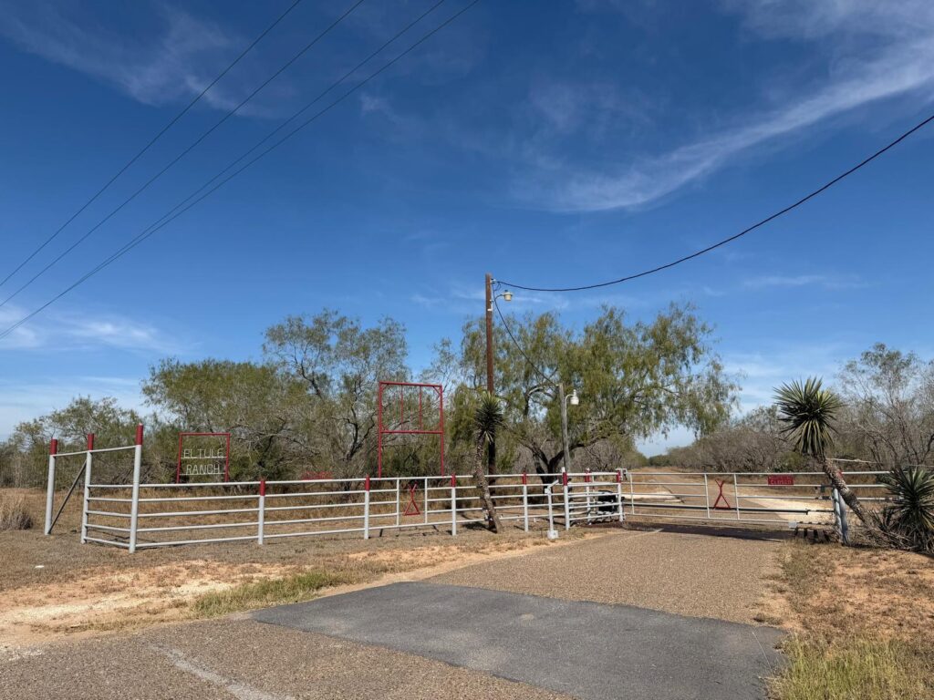 Puerta y valla a la entrada del rancho El Tule, en el norte del condado de Hidalgo, que muestran los terrenos del rancho sin urbanizar bajo un cielo despejado.