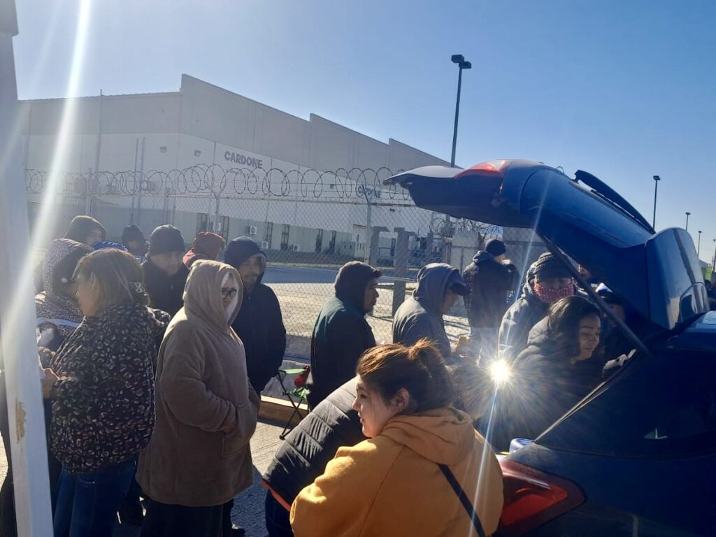 Workers bundled in jackets and hoodies line up outside a fenced Cardone auto parts plant in Matamoros during the morning.