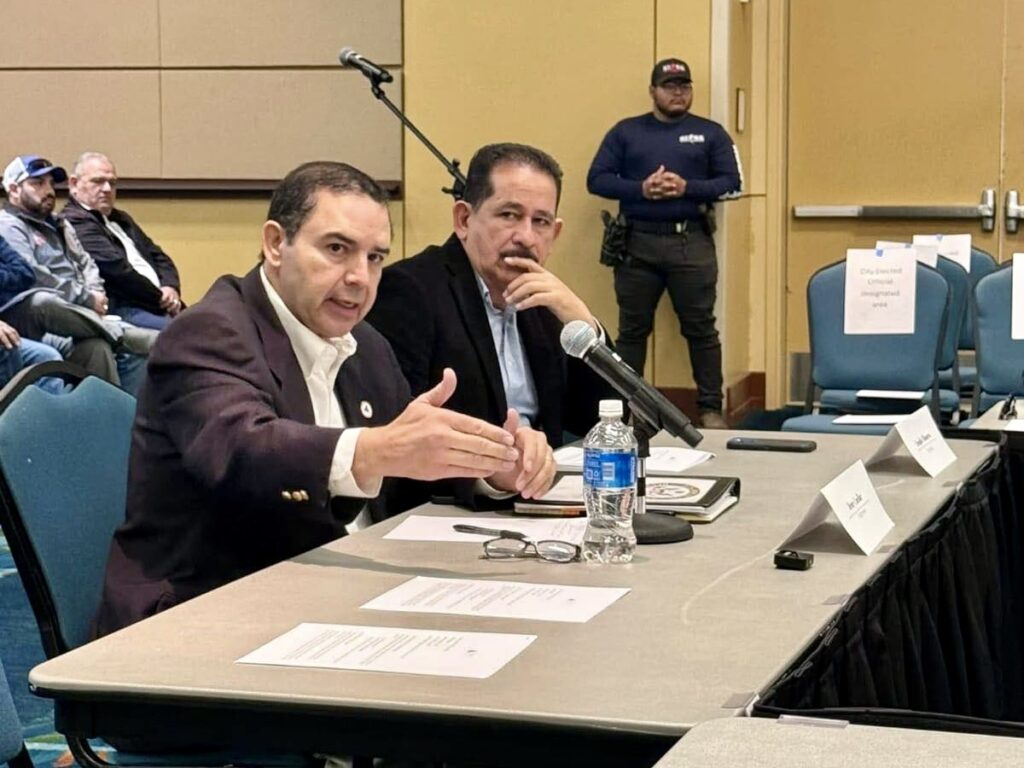 U.S. Rep. Henry Cuellar speaks into a microphone while seated at a table during a South Texas Builders Association meeting.