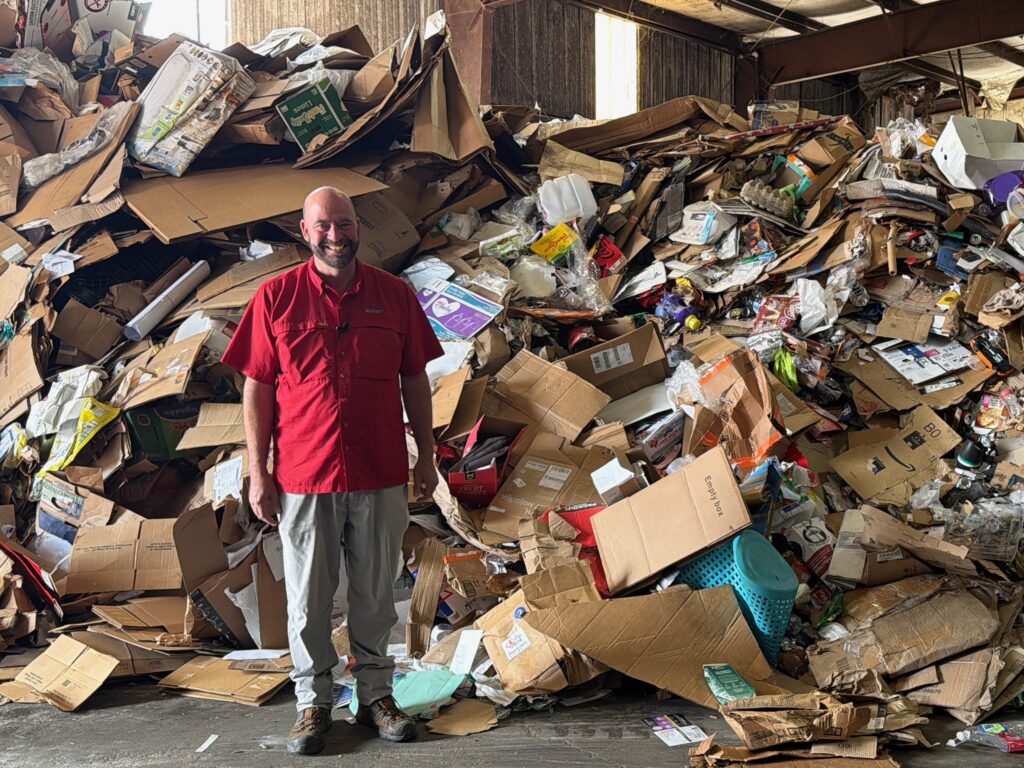 A man standing in front a recycling in a red shirt.