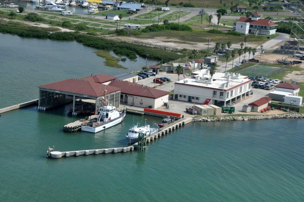 Vista aérea de la estación de la Guardia Costera de EE. UU. en South Padre Island, con muelles, embarcaciones e instalaciones portuarias a lo largo de la costa del Golfo.