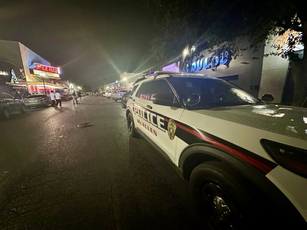 A McAllen police SUV parked on a downtown street at night with bars, neon signs, and pedestrians in the background.