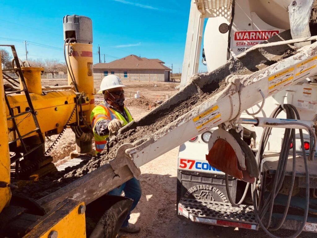 A construction worker wearing a hard hat and safety vest controls a concrete chute during a pour.
