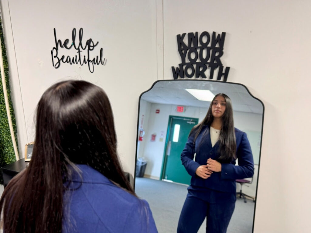 Student wearing a navy suit looks at her reflection in a mirror inside South Texas College’s Threads Career Closet.
