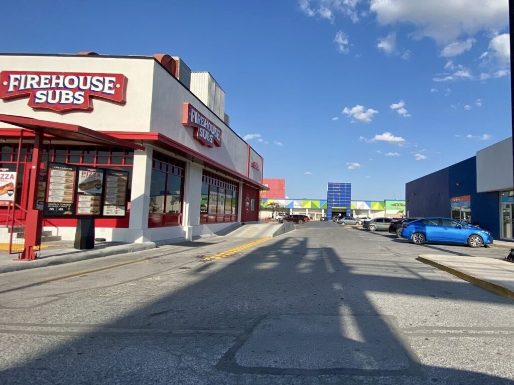 Retail strip in Reynosa with restaurants and parked cars during normal business hours.