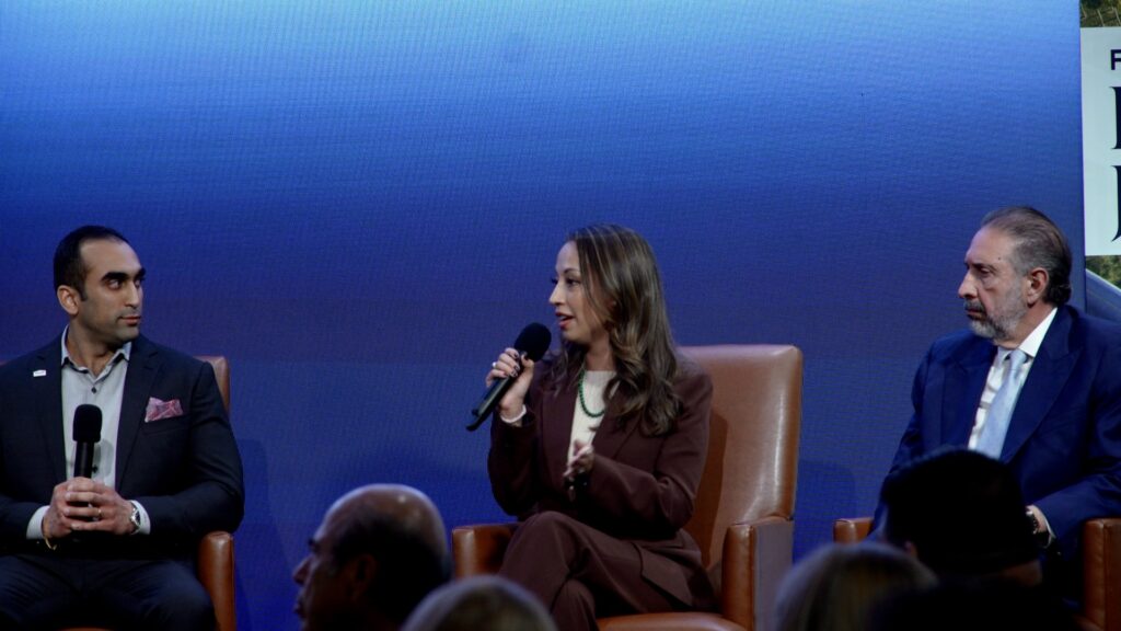 Andrea Figueroa Benton speaks into a handheld microphone while seated on stage during the Rio Grande Valley Business Journal’s 2026 Economic Outlook event, with Shant Samtani and Joaquin Spamer seated on either side of her.