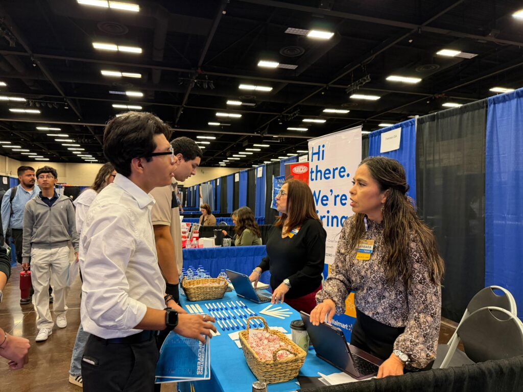 A recruiter speaks with a young man at a booth with hiring signs and informational materials during the McAllen career fair.