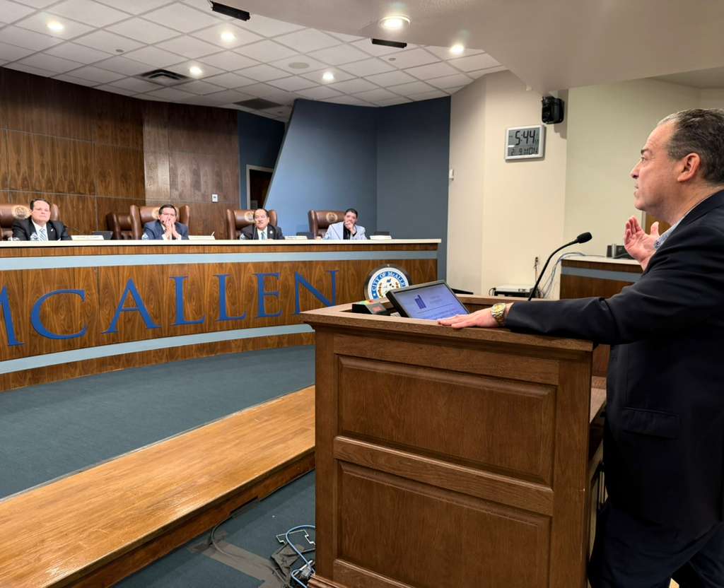 Michael Fallek stands at a podium inside McAllen City Hall, speaking to city commissioners seated at the dais during a public meeting about the former Civic Center redevelopment project.