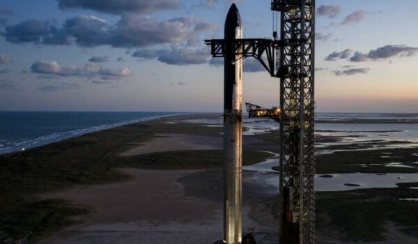 A SpaceX Starship rocket stands upright on its launch pad near the South Texas coastline at sunset, with wetlands and the Gulf visible in the background.