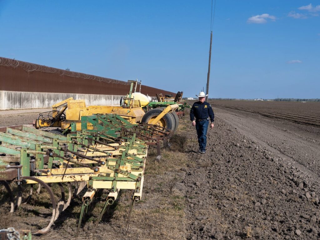 Texas Ag Commissioner Sid Miller walks next to farm equipment and the border wall.