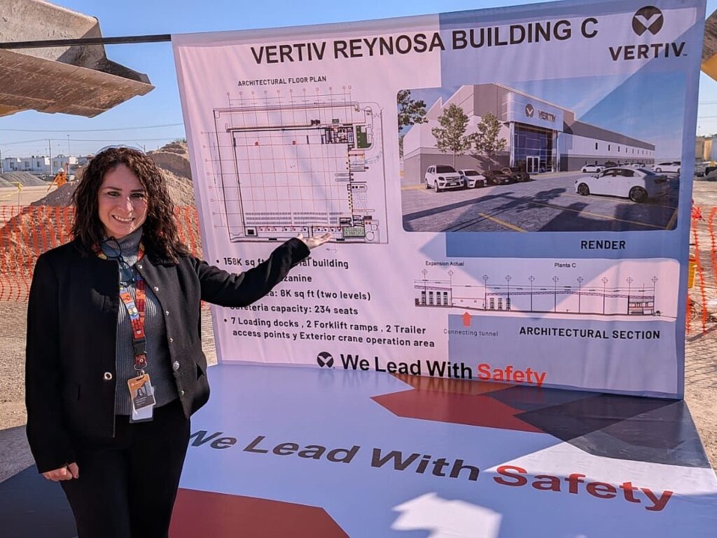 A Vertiv project leader stands in front of a large display board showing floor plans and a rendering of the new Vertiv Reynosa Building C at a construction site.