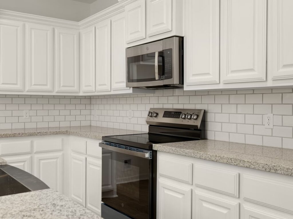 Cocina con armarios blancos, salpicadero de azulejos y horno y microondas de acero inoxidable.