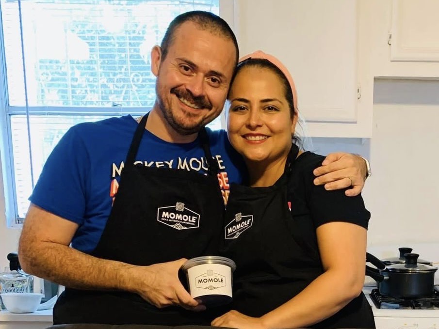 Los fundadores de omole, Gustavo Adolfo Gutiérrez Reyes y Jocelyn Guerrero Enríquez, posan en una cocina con un recipiente de mole en la mano.