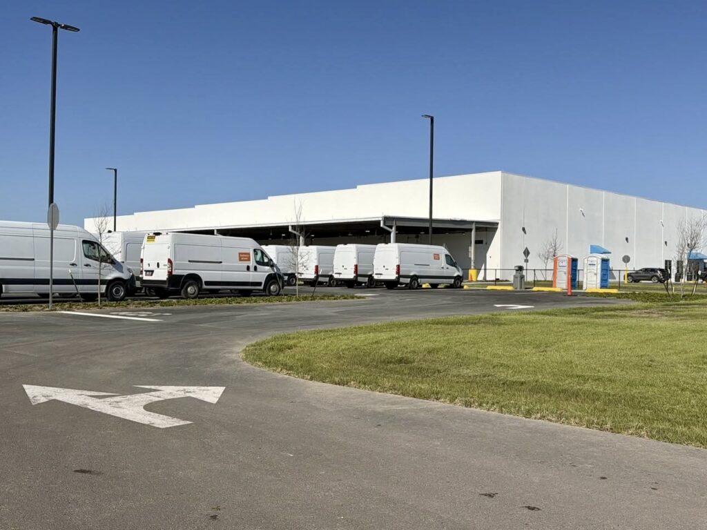 Furgonetas de reparto blancas aparcadas frente a un almacén con muelles de carga en las instalaciones de Amazon en Brownsville.