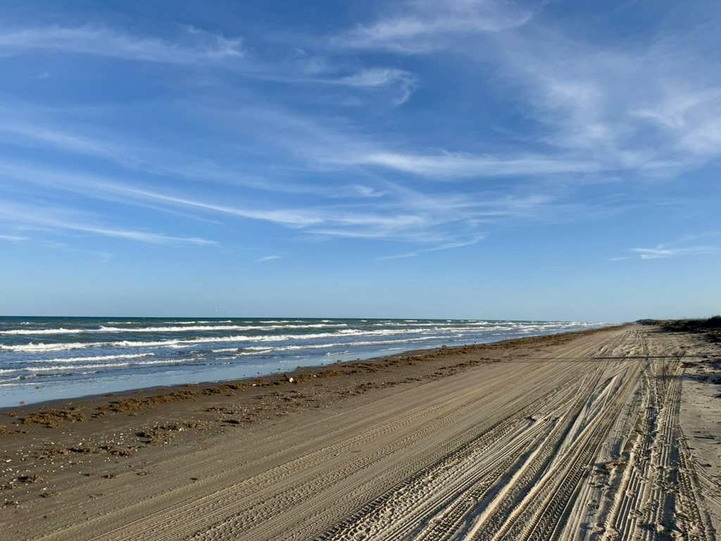 Wide view of Boca Chica Beach shoreline with waves, sand, and tire tracks along the coast