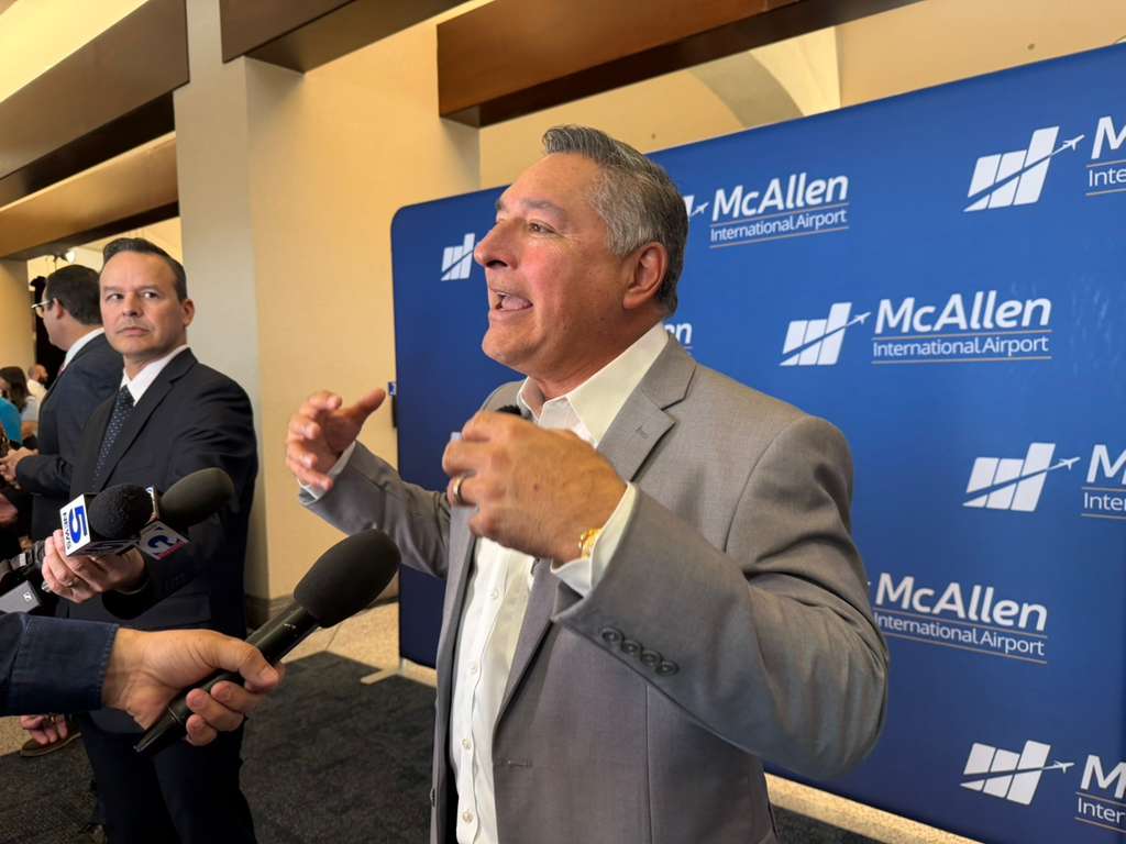 McAllen Mayor Javier Villalobos speaks to reporters in front of a McAllen International Airport backdrop during an announcement about a new nonstop flight to Monterrey.