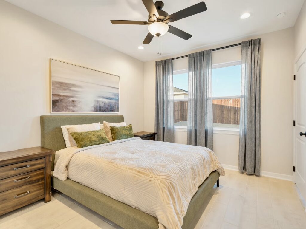 Dormitorio con cama, mesitas de noche, ventilador de techo y ventana con cortinas.