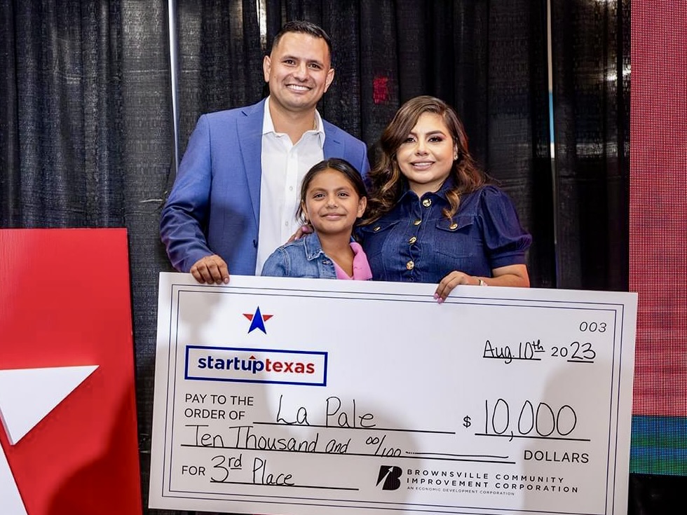 Gerardo and Daisy Alcazar and their daughter hold a large $10,000 Startup Texas award check onstage at a pitch competition in Brownsville.